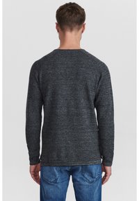 Grå stickad tröja med långa ärmar och texturerad yta, rund halsringning och ribbade manschetter, i kombination med blå jeans. Vy från baksidan.