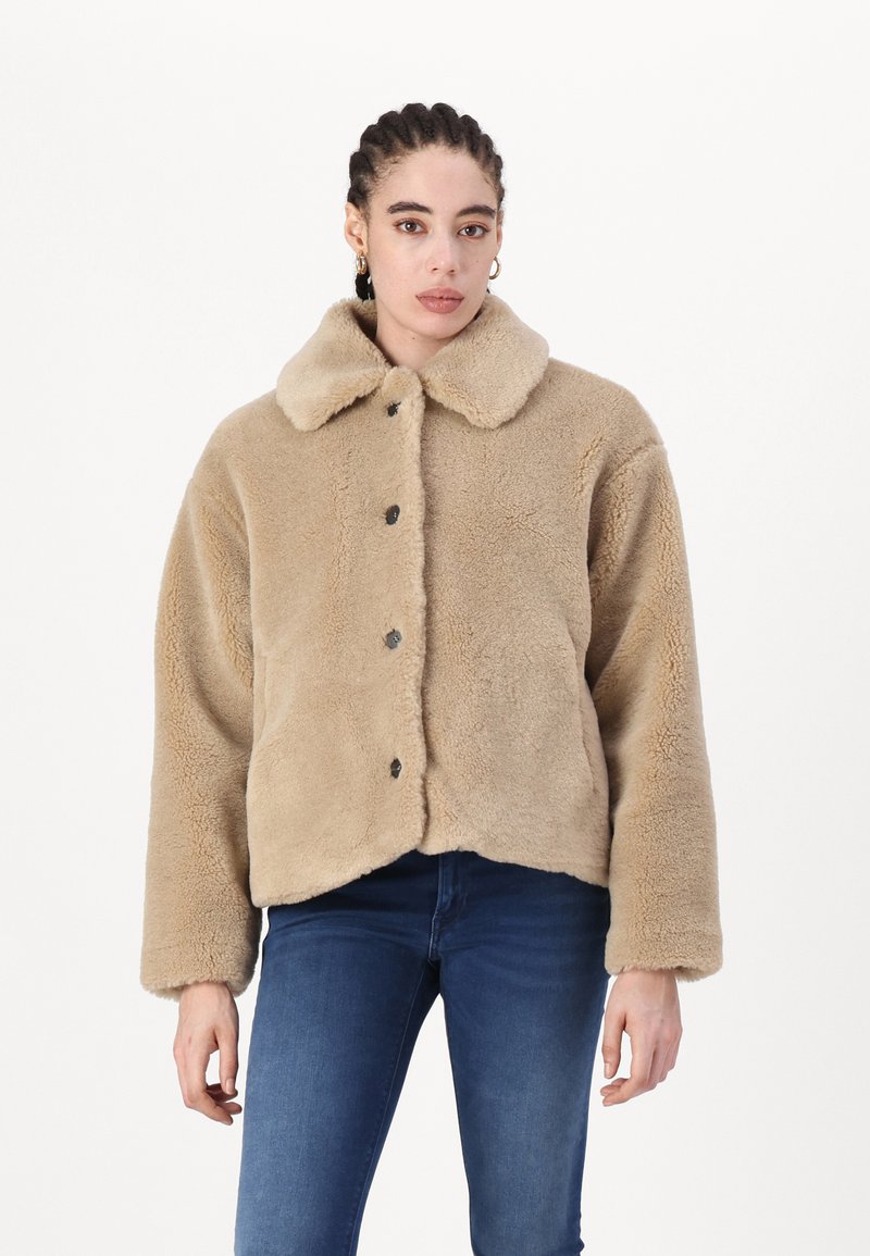 Beige kunstpelsjakke med kragesnitt, frontknapper og lange ermer, med et kort design og myk tekstur.