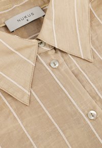 Beige overhemd met korte mouwen, gekenmerkt door witte verticale strepen, een puntkraag en twee knoopsluitingen van textuurstof. Merklabel zichtbaar.
