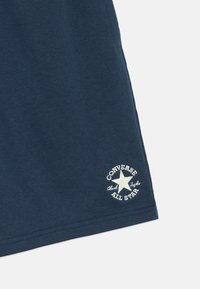 Μπλε σκούρο μπλουζάκι από βαμβάκι, με κυκλικό λευκό λογότυπο "Converse All Star" με λεπτομέρεια αστέρι στο τελείωμα.