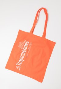 Sac tote en coton orange avec de longues poignées, comportant un texte imprimé blanc et un logo. Tissu léger et design rectangulaire simple.