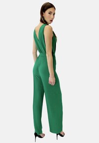 Mono acampanado verde con diseño sin mangas, espalda en V profunda y cintura ajustable. Combinado con tacones altos negros y pendientes de plata.