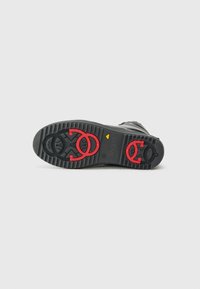 Sole in gomma nera con superficie testurizzata. Presenta accenti circolari rossi e un indicatore giallo. Resistente, progettata per trazione e stabilità.