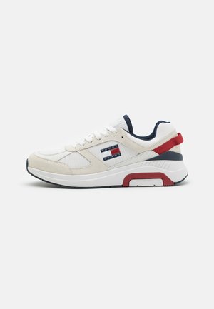 Zapatilla blanca con parte superior de ante y tejido, acentos en azul marino, lengüeta trasera roja y un logo de marca en el lateral. Presenta una suela acolchada para mayor comodidad.