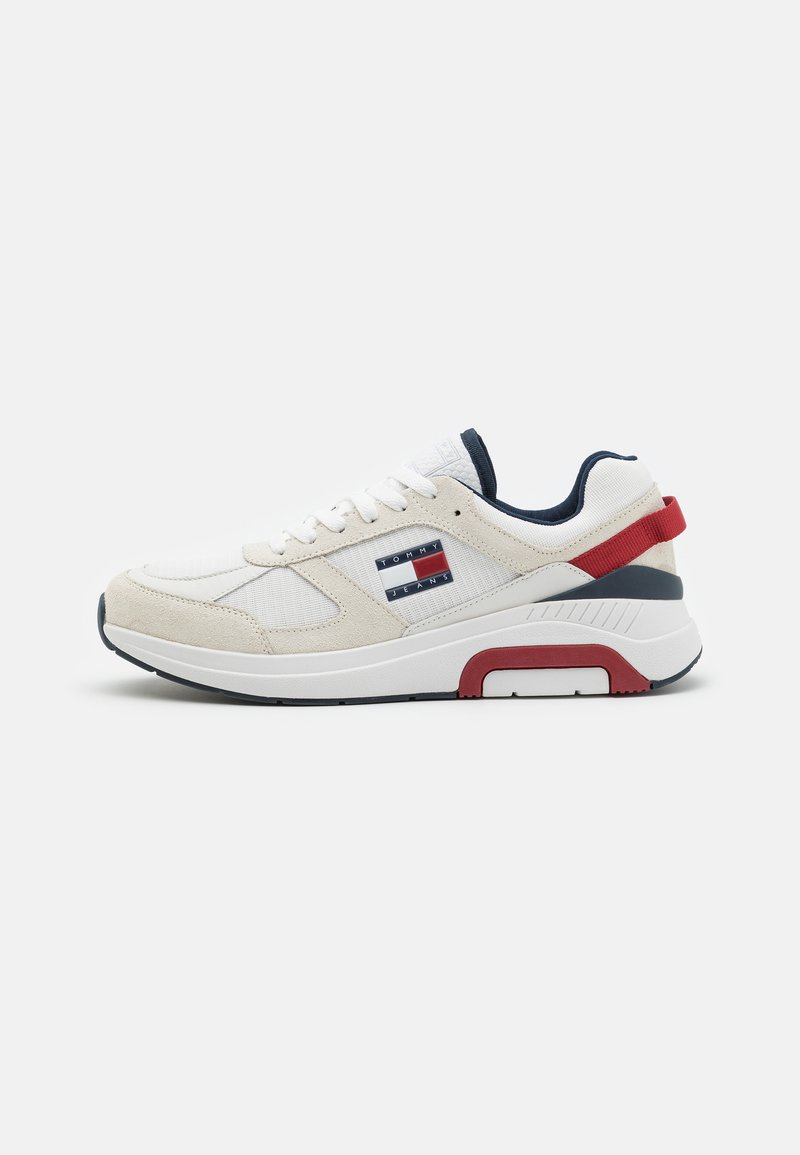 Zapatilla blanca con parte superior de ante y tejido, acentos en azul marino, lengüeta trasera roja y un logo de marca en el lateral. Presenta una suela acolchada para mayor comodidad.