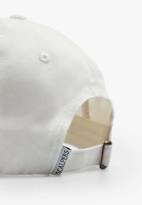 Gorra de béisbol de algodón blanco con una correa de ajuste de metal en la parte trasera y una pequeña etiqueta de tela con la etiqueta "SCALPERS".
