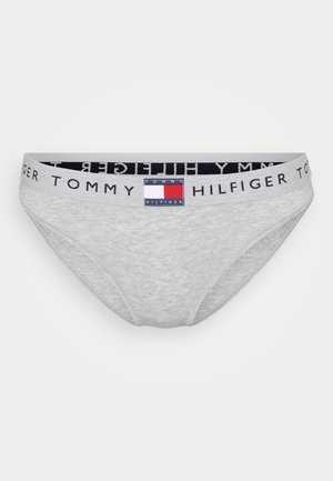 Pilkos medvilnės kelnaitės su tamsia diržo juosta, ant kurios užrašyta "TOMMY HILFIGER", ir spalvotu logotipo ženkleliu priekyje.