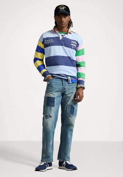 Polo a maniche lunghe a righe in azzurro chiaro, blu navy, verde e giallo; jeans blu strappati con toppe; sneakers blu navy; cappellino nero con logo.