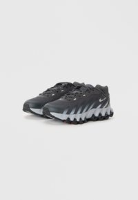 Chaussures de sport noires avec une tige texturée, des accents gris et un design de semelle unique et segmenté avec un rembourrage visible et un logo Nike.