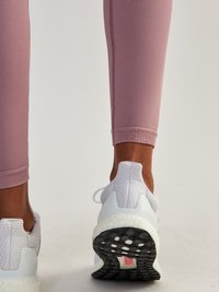 Light pink athletic leggings with textured fabric and seams, paired with white and gray running shoes featuring a patterned rubber sole.