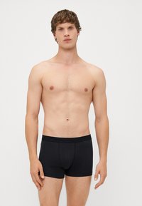 Černé bavlněné boxerky s přiléhavým střihem, elastickým pasem a bezšvovým předním vakem. Model stojí bez trička na neutrálním pozadí.