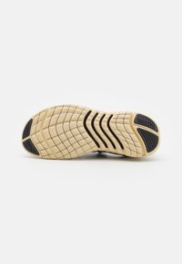 Semelle de chaussure beige avec des patchs de grip noirs au talon et à l'orteil, et des rainures ondulées noires au niveau du midfoot.