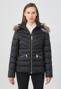 Jachetă neagră matlasată cu glugă din blană sintetică, fermoare aurii și două buzunare cu fermoar. Prezintă un design matlasat și o siluetă ajustată.