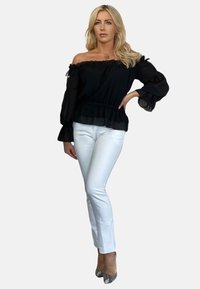 Czarna bluzka bez ramion z falbaniastymi rękawami, zestawiona z dopasowanymi białymi spodniami i wzorzystymi obcasami. Prosty, elegancki design.