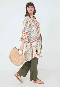 Patterned lightweight kimono with floral and rainbow motifs, featuring wide sleeves, a tie waist, paired with olive green pants and a woven bag.