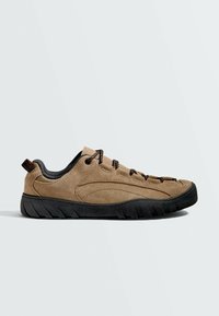 Chaussure décontractée en daim marron clair avec semelle noire et lacets noirs, vue de profil sur un fond clair uni.