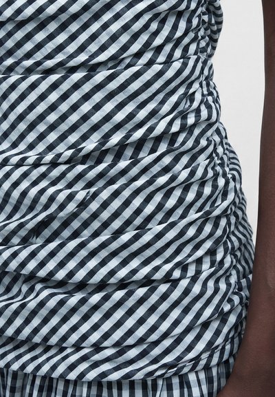 Τμήμα υφάσματος σε άσπρο-μαύρο καρό με ρυτίδες φορεμένο σε σκούρο δέρμα μπράτσο πάνω σε άσπρο φόντο.