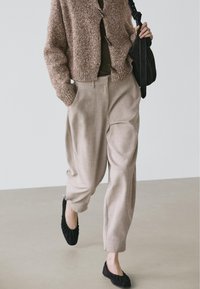 Tekstureret brun strikket cardigan, olivengrøn top, beige bukser med vide ben og sidelommer samt sorte flade sko, velegnet til afslappet brug.