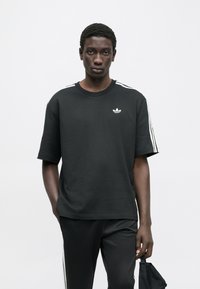 Μαύρο βαμβακερό κοντομάνικο μπλουζάκι με λευκές ρίγες στους ώμους και μικρό λευκό λογότυπο στο στήθος.