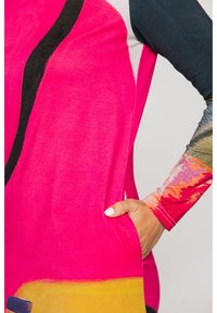 Túnica colorida que presenta tela rosa brillante, patrones abstractos, mangas largas con texturas variadas y un bolsillo lateral para mayor funcionalidad.