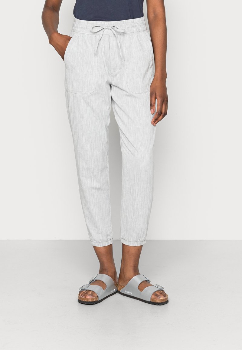 Jasnoszare, lekkie spodnie z elastycznym pasem, sznurkiem do regulacji, bocznymi kieszeniami i zwężanymi nogawkami. Noszone z szarymi sandałami.