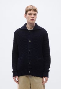 Tengerészkék kötött kardigán bord�ázott textúrával, nagy gallérral és három elülső gombbal. Két elülső zsebbel és bordázott mandzsettákkal rendelkezik.