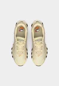 Beige Nike Air Max sporta apavi ar auklām, redzama Air Max amortizācija un mazs oranžs Nike zīmols uz pirksta zonas, skats no augšas.