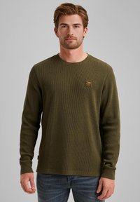 Chemise à manches longues vert olive en tissu texturé, avec un col rond, un petit logo brodé sur la poitrine et une coupe décontractée.