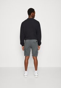 Grå cargo shorts med sidelommer, kombinert med en marineblå langermet genser. Modellen vender bort, noe som fremhever lomme detaljer og stoff tekstur.