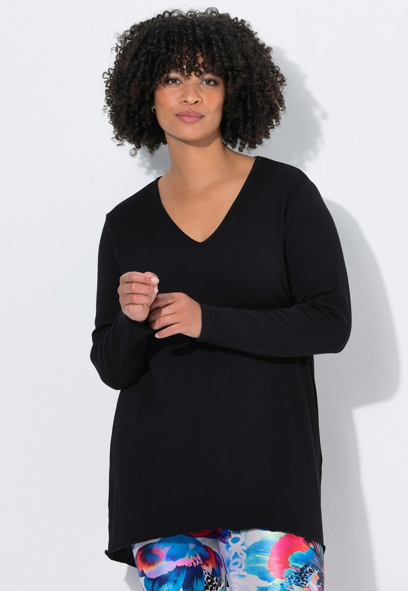 Schwarzes Langarmoberteil mit V-Ausschnitt, locker sitzend und aus weichem Material. Dazu werden bunte, gemusterte Leggings getragen.