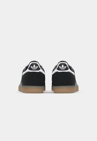 Juodos ir baltos sportinės bateliai su tekstūruota juoda viršutine dalimi, baltais akcentais ir guminiu padu. Ant kulno yra Adidas logotipas.