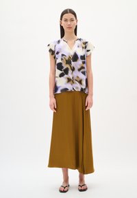 Blouse multicolore à manches courtes, avec un motif de violets et de noirs, associée à une longue jupe jaune moutarde unie et des sandales noires.