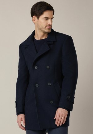 Granatowy wełniany płaszcz z podwójnym zapięciem, dużymi czarnymi guzikami, kołnierzem z wycięciem i bocznymi kieszeniami. Teksturowany materiał dodaje ciepła.