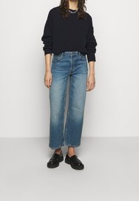 Blue jeans with a straight-leg cut, faded at the thighs, paired with a black long-sleeve sweater and black chunky loafers.