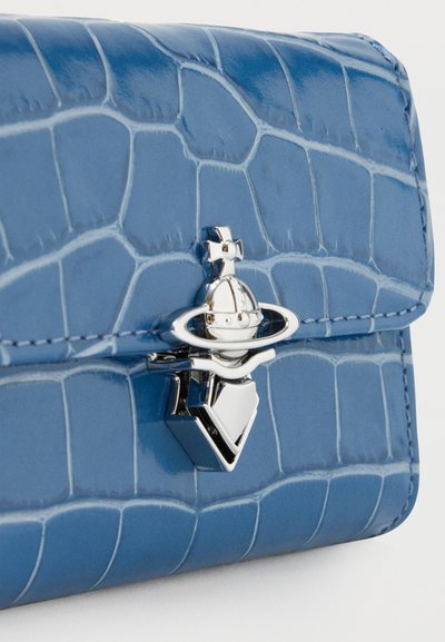 Portefeuille en cuir bleu à texture crocodile avec un fermoir orbe argenté brillant évoquant Saturne, surmonté d'une croix.