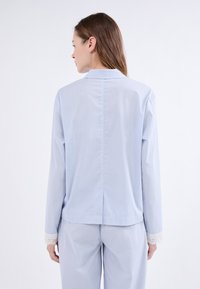Camisa de pijama a rayas azul claro con mangas largas, cuello y acentos de encaje en los puños. La parte trasera presenta un corte recto y una costura central.
