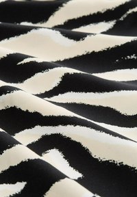 Tessuto nero con strisce irregolari color crema, dalla texture morbida e una finitura leggermente lucida, creando un contrasto audace nel motivo.