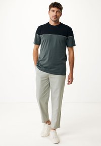 Camiseta colorblock en gris y negro con mangas cortas, combinada con pantalones gris claro. Zapatillas blancas completan el conjunto. Diseño simple y casual.