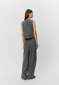 Grauer, taillierter Weste und weit geschnittenen Hosen, beide aus einem glatten, strukturierten Stoff, mit minimalen Nähten und einer lässigen Silhouette.