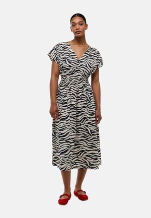 Robe blanche avec imprimé zèbre noir, en V, manches courtes flottantes, taille cintrée et jupe fluide ; associée à des chaussures rouges.