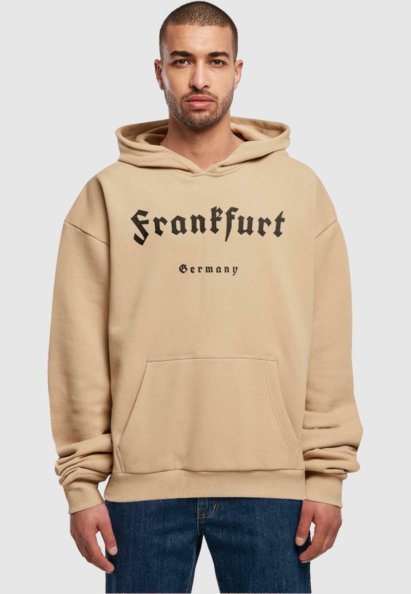 Haut de survêtement beige avec une poche kangourou, arborant le texte noir "Francfort" et "Allemagne" imprimé en gras. Mélange de coton, coupe décontractée.