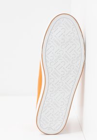 Semelle d'une basket orange avec une bande de caoutchouc blanche à motif de texte et logos "ESPRIT", taille 37 indiquée près de l'avant-pied.