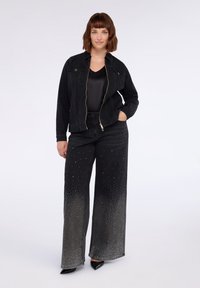 Mustat denimpuserot, joissa on vetoketju edessä, yhdistettynä mustiin leveälahkeisiin housuihin, joissa on gradienttimuotoilu ja hopeiset niittikoristeet.