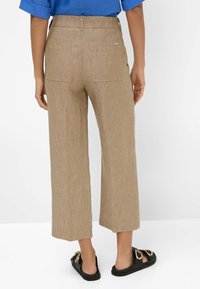 Bruine linnen wijde broek met een elastische tailleband, twee achterzakken met een patch en een ontspannen pasvorm, gecombineerd met zwarte instapsandalen.