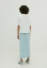 Witte kortebloes t-shirt gecombineerd met een lichtblauwe denim maxi rok, met een rechte snit en twee achterzakken, gedragen met lichtblauwe hakken.