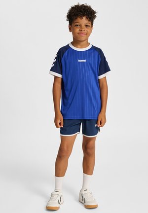 Blå randig sportskjorta med marinblå ärmar, kombinerad med marinblå shorts med vit kant. Komplett med vita strumpor och ljusa sneakers.