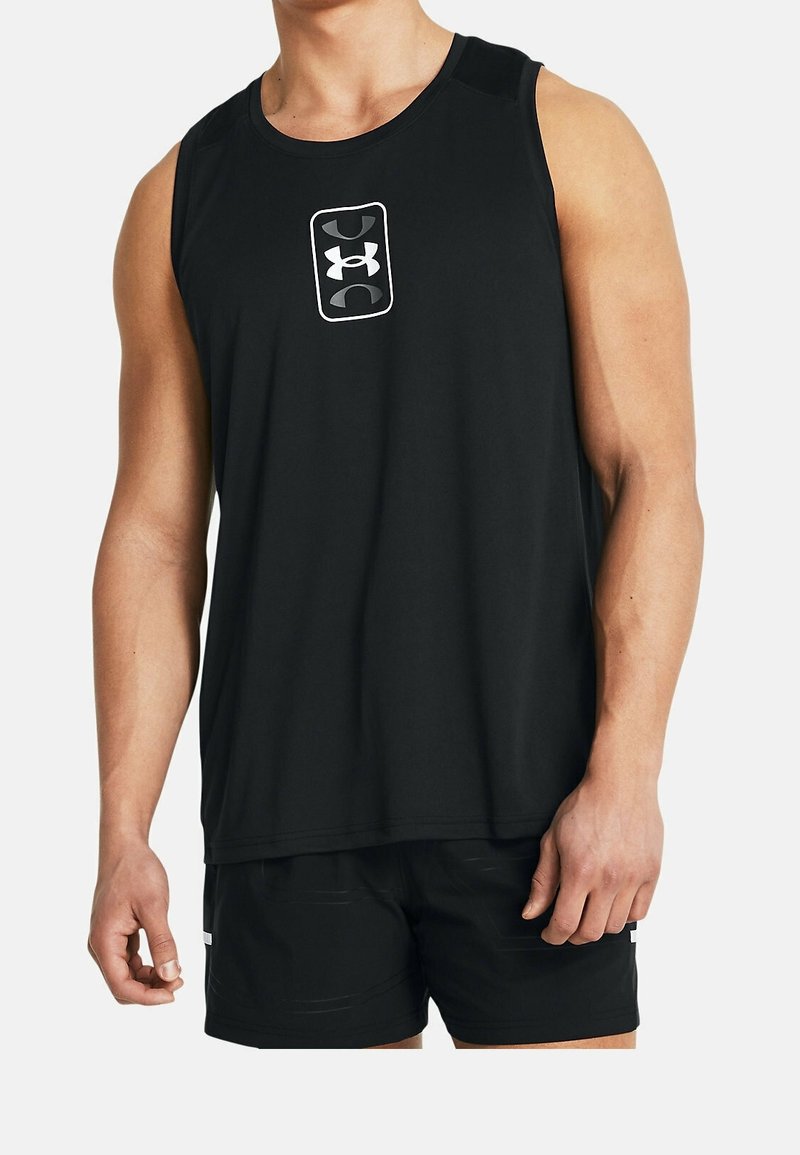 Homme portant un débardeur de sport noir avec un logo blanc et un short noir, debout devant un fond clair uni.