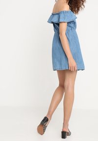 Jeansklänning med bar axel och volangkant vid halsen, manschetter vid midjan och längd ovanför knäna. Har en mjuk textur och en avslappnad passform.