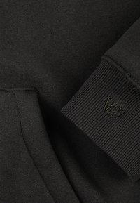 Tamnosiva majica s mekanom teksturom, rebrastim manžetnama i malim utisnutim logotipom u malo svjetlijoj nijansi.