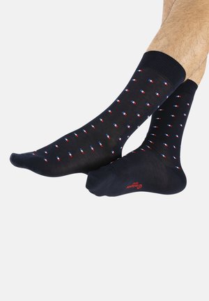 Chaussettes noires avec des motifs rectangulaires rouges et bleus, cuffs côtelés, et détails de logo rouges au niveau des orteils. Texture de tissu lisse.